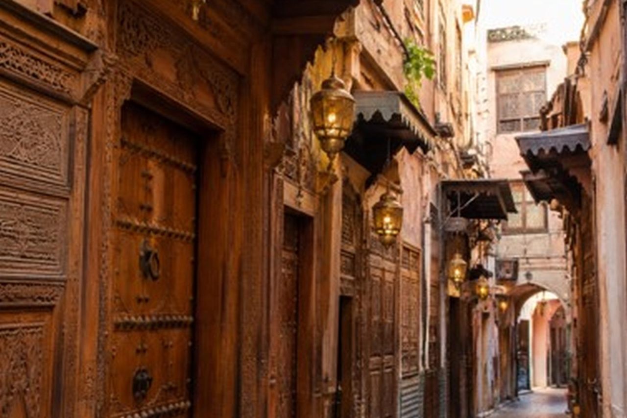 Narrow lane of the Fes medina lined with carved wooden doorways and brass lanterns